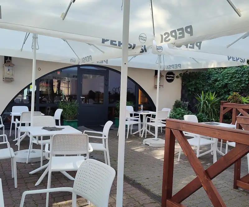 Ogródek pizzerii z białymi parasolami i drewnianą balustradą