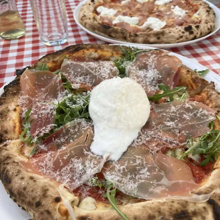 Pizza Parma z całą burratą, szynką parmeńską i rukolą na obrusie w kratkę